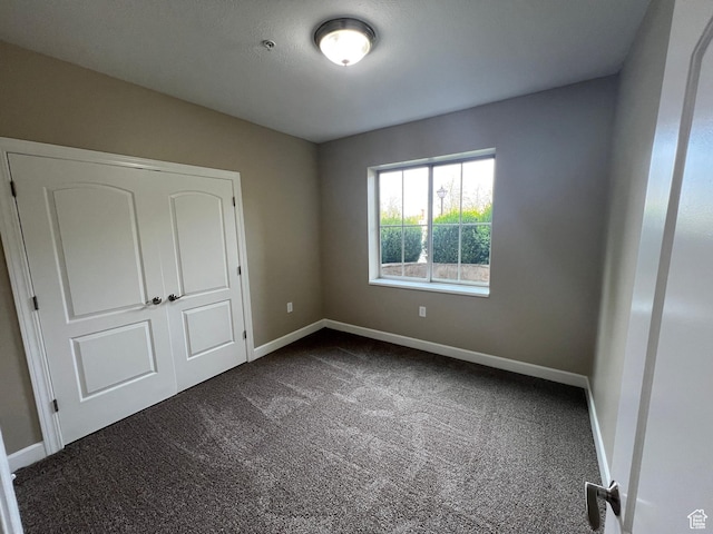 unfurnished bedroom with dark colored carpet and baseboards