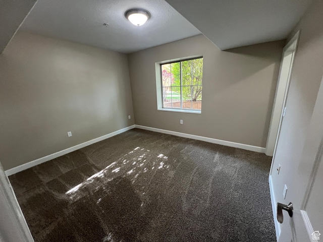 spare room featuring dark carpet and baseboards