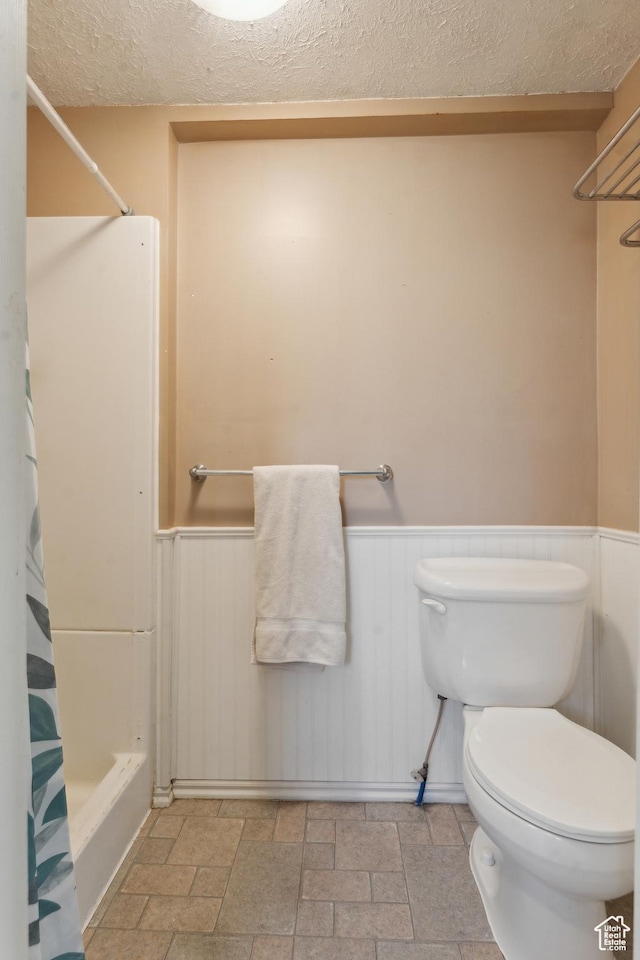 755 42nd St, South Ogden, UT 84403 - full bathroom with a textured ceiling, a wainscoted wall, toilet, stone finish flooring, and shower / bath combo with shower curtain