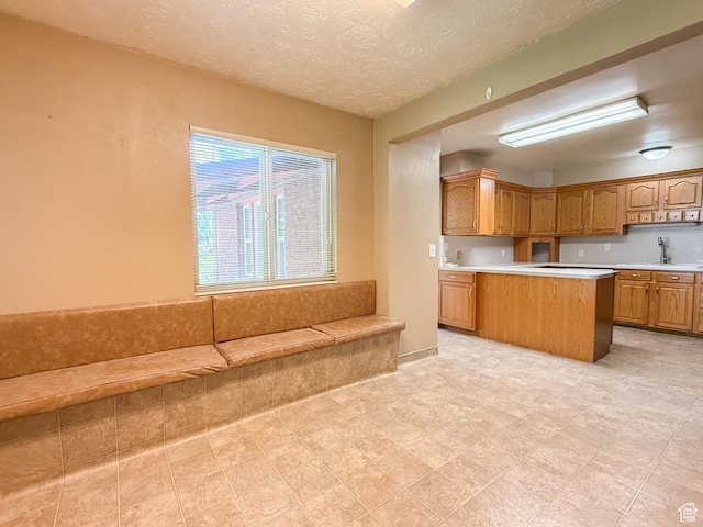 kitchen featuring light countertops, a sink, brown cabinetry, and a textured ceiling
