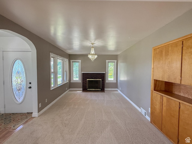 unfurnished living room with a fireplace, arched walkways, baseboards, light carpet, and a chandelier