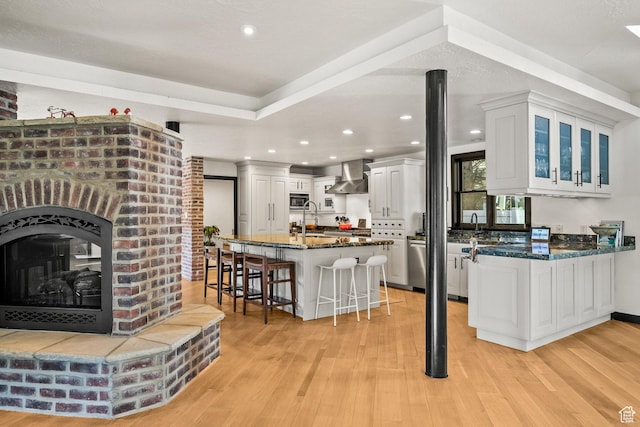 kitchen featuring wall chimney exhaust hood, stainless steel appliances, a breakfast bar area, a sink, and light wood finished floors