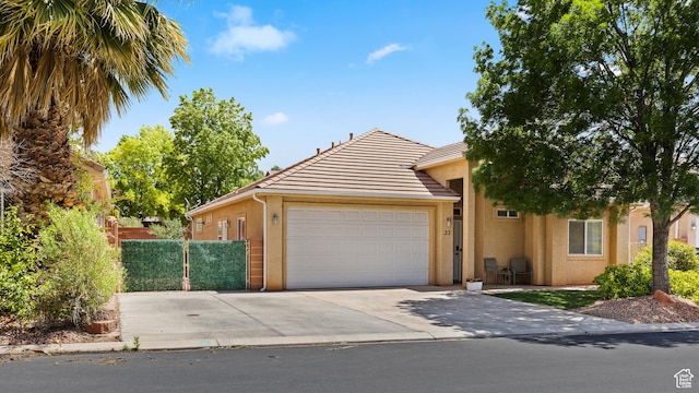 view of front of property featuring stucco siding, an attached garage, a tiled roof, driveway, and fence