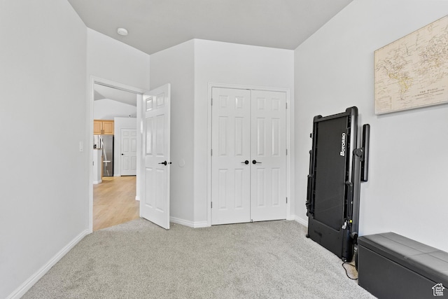 unfurnished bedroom featuring light carpet, freestanding refrigerator, baseboards, and a closet