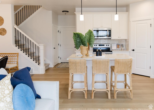 kitchen featuring appliances with stainless steel finishes, light wood-style flooring, tasteful backsplash, a center island, and light countertops
