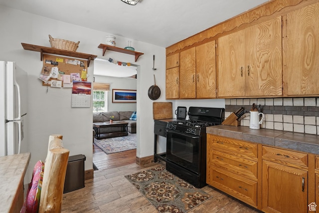 kitchen featuring gas stove, freestanding refrigerator, wood-type flooring, tasteful backsplash, and dark countertops