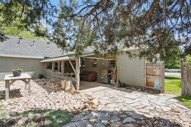 rear view of house featuring driveway, a patio, and roof with shingles