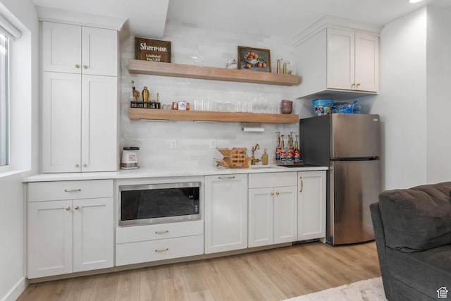 indoor bar featuring stainless steel appliances, decorative backsplash, and light wood-style flooring