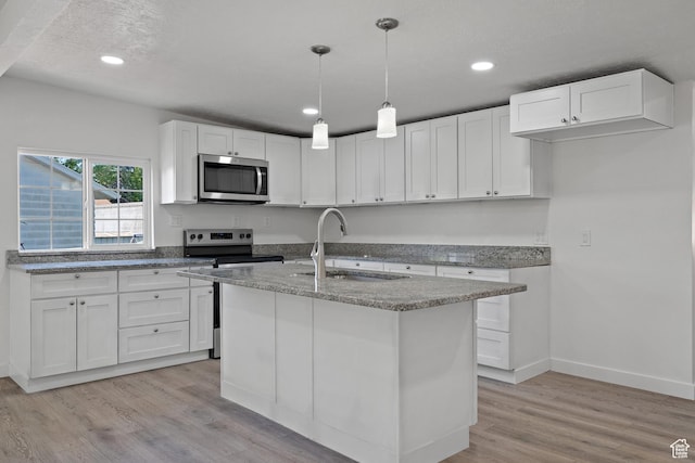 kitchen featuring appliances with stainless steel finishes, a sink, light wood-style flooring, light stone counters, and white cabinets
