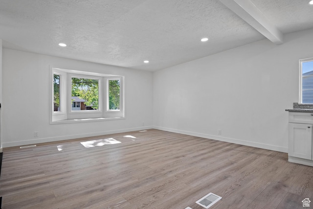 unfurnished room featuring a textured ceiling, light wood finished floors, beamed ceiling, recessed lighting, and baseboards