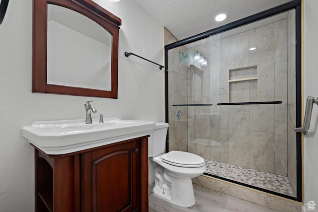 bathroom featuring toilet, a stall shower, vanity, a textured ceiling, and wood finished floors