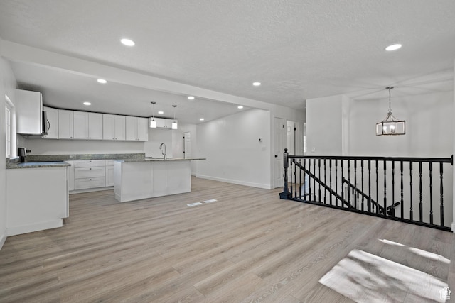 kitchen with recessed lighting, light wood finished floors, white cabinetry, a chandelier, and a center island with sink