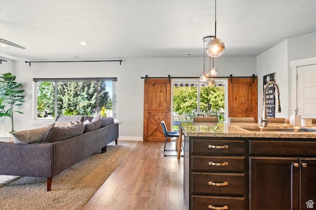 kitchen with a barn door, a sink, open floor plan, dark brown cabinets, and light wood-style flooring