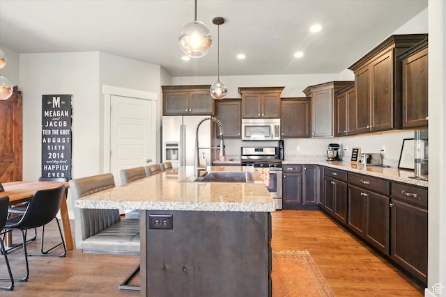 kitchen featuring appliances with stainless steel finishes, a breakfast bar, dark brown cabinets, an island with sink, and recessed lighting