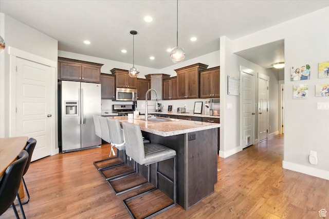 kitchen with stainless steel appliances, a sink, a kitchen island with sink, dark brown cabinetry, and a kitchen breakfast bar