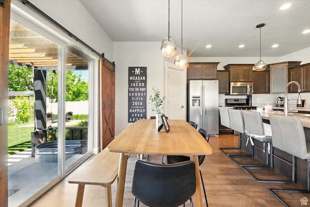 dining space featuring a barn door, light wood-type flooring, and recessed lighting