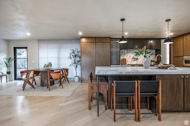 4279 S Lares Cir, Salt Lake City, UT 84124 - kitchen featuring a breakfast bar area, oven, light wood-style floors, light stone countertops, and decorative light fixtures