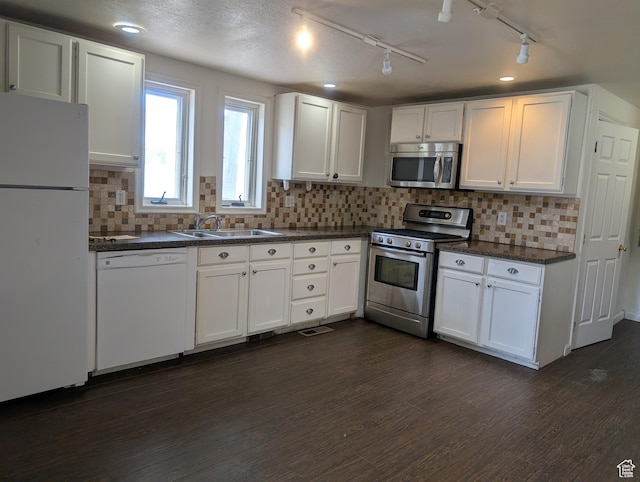 kitchen with appliances with stainless steel finishes, a sink, dark countertops, white cabinetry, and dark wood-style flooring