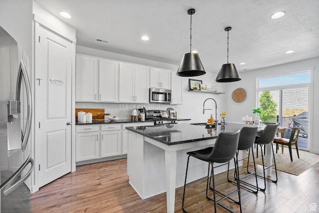 kitchen with stainless steel appliances, a sink, white cabinets, light wood finished floors, and a kitchen island with sink