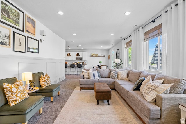 living area featuring recessed lighting, light carpet, a decorative wall, and wainscoting