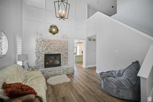 living area with a high ceiling, wood finished floors, a chandelier, a fireplace, and baseboards