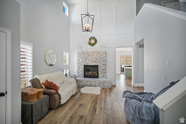 living area with a high ceiling, wood finished floors, a chandelier, and a stone fireplace
