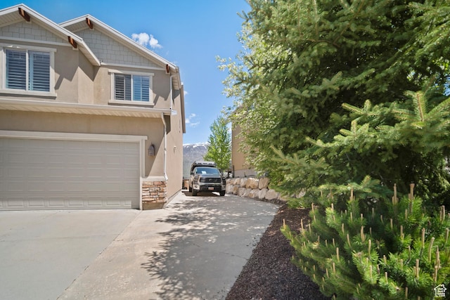 view of side of property with stucco siding, concrete driveway, an attached garage, and stone siding
