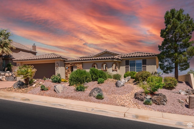 mediterranean / spanish-style home featuring stucco siding, a tile roof, and an attached garage