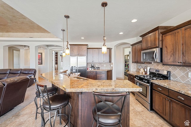 kitchen with appliances with stainless steel finishes, arched walkways, a sink, open floor plan, and a kitchen breakfast bar