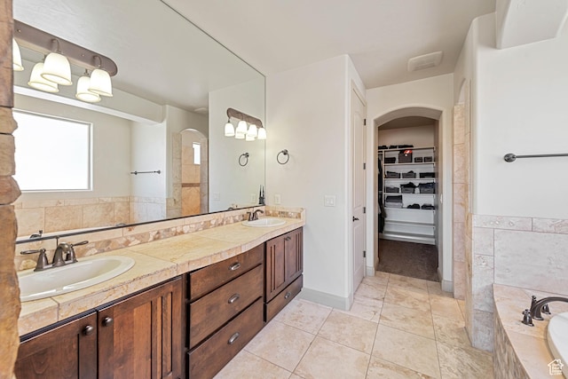 bathroom with double vanity, tiled tub, a walk in closet, and tile patterned floors