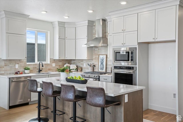 kitchen with appliances with stainless steel finishes, a sink, wall chimney range hood, light wood-style floors, and decorative backsplash