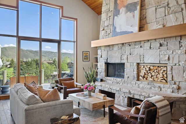 living room with a stone fireplace, high vaulted ceiling, wood finished floors, wooden ceiling, and a mountain view