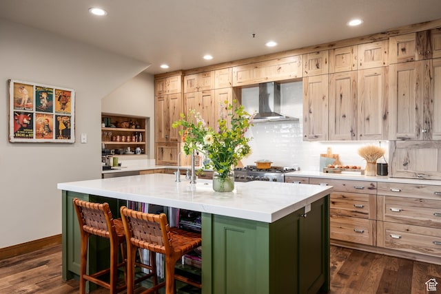 kitchen featuring wall chimney range hood, dark wood finished floors, recessed lighting, a kitchen island with sink, and tasteful backsplash