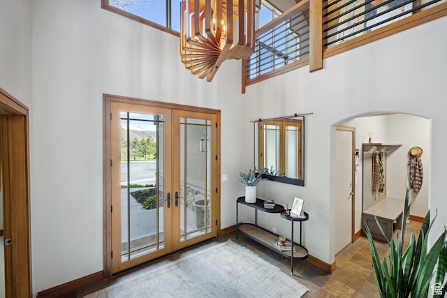 entryway with a towering ceiling, french doors, stone finish floors, baseboards, and arched walkways