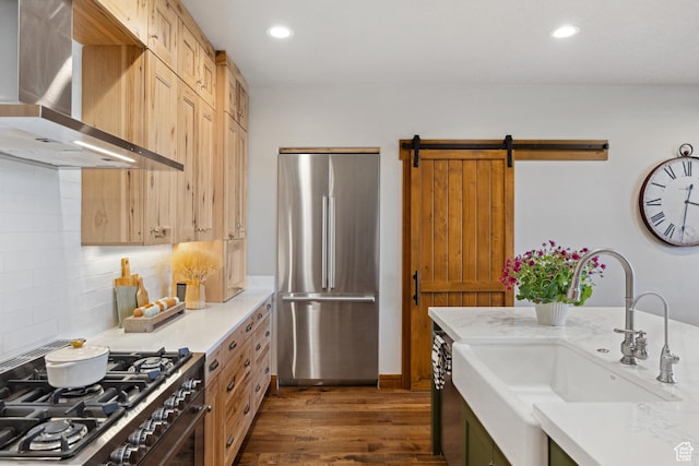 kitchen featuring appliances with stainless steel finishes, wall chimney range hood, a sink, dark wood-style flooring, and light countertops
