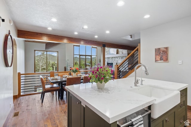 kitchen with a sink, recessed lighting, light wood-type flooring, light stone counters, and a textured ceiling