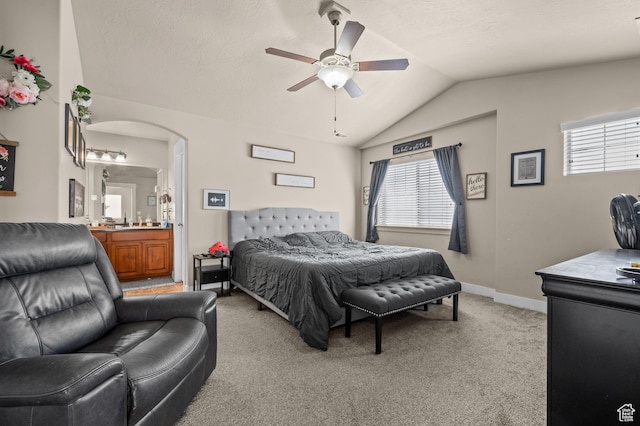 bedroom with lofted ceiling, light colored carpet, arched walkways, ensuite bathroom, and a ceiling fan