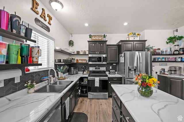 kitchen with appliances with stainless steel finishes, open shelves, a sink, light wood-type flooring, and decorative backsplash