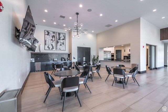 dining space with a towering ceiling, recessed lighting, a chandelier, light tile patterned floors, and baseboards
