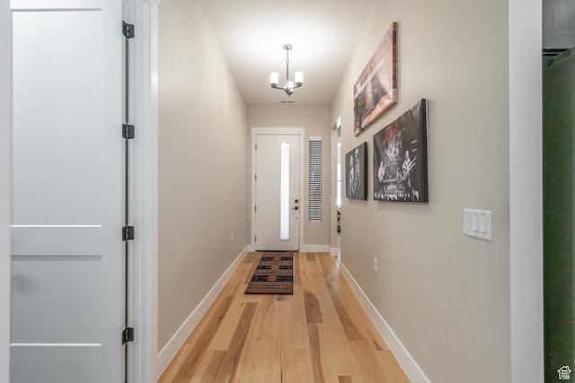 doorway to outside with light wood-type flooring, a chandelier, and baseboards