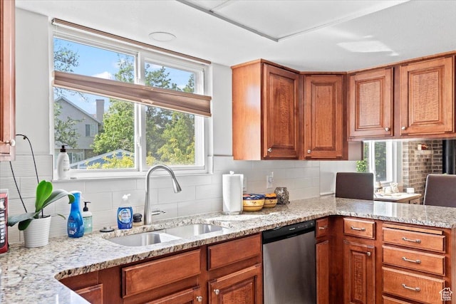 kitchen with dishwasher, a sink, tasteful backsplash, brown cabinetry, and light stone counters