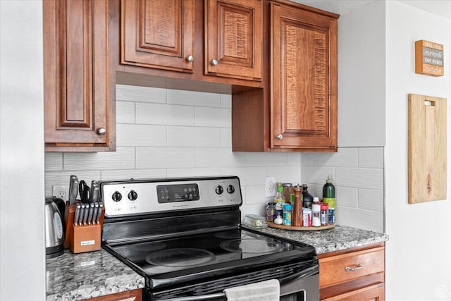kitchen featuring stainless steel electric range, backsplash, light stone countertops, and brown cabinetry