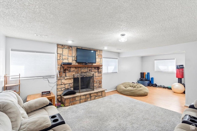 living room featuring a stone fireplace, a textured ceiling, and wood finished floors