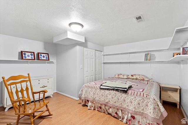 bedroom with light wood-type flooring, a closet, a textured ceiling, and baseboards