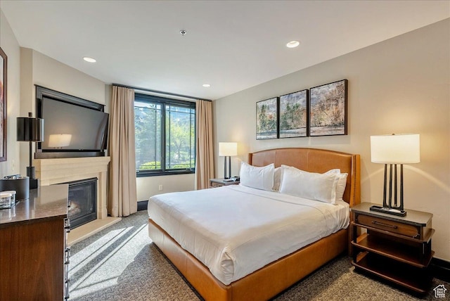 carpeted bedroom featuring a glass covered fireplace, recessed lighting, and baseboards