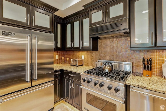 kitchen featuring high end appliances, tasteful backsplash, light stone countertops, and dark brown cabinets