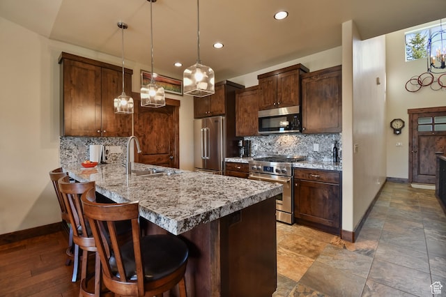kitchen with high end appliances, a sink, baseboards, a peninsula, and backsplash