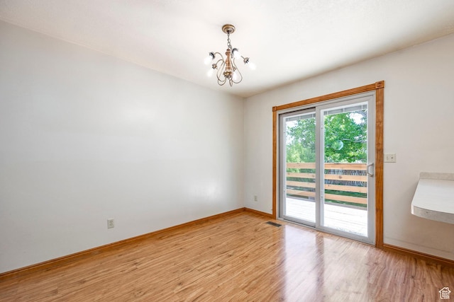 unfurnished room featuring a chandelier, light wood finished floors, and baseboards