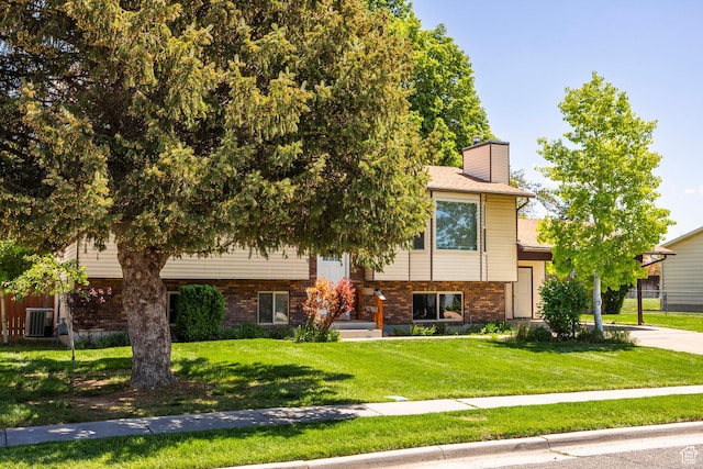 view of front of property featuring a front yard, a chimney, brick siding, and central AC
