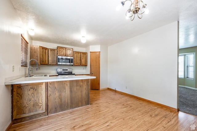kitchen featuring appliances with stainless steel finishes, a sink, light countertops, light wood-style flooring, and a chandelier